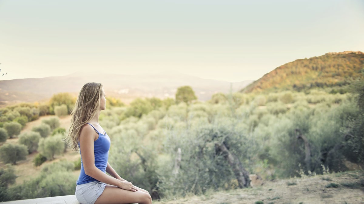 A woman in casual attire sits peacefully, enjoying a scenic outdoor view of nature.